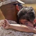 In the aftermath of a disaster a little girl peers over the shoulder of a soldier.